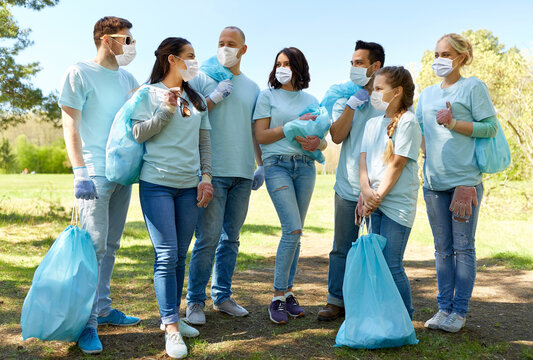 volunteering, health and ecology concept - group of volunteers wearing face protective medical mask for protection from virus disease with garbage bags talking in park
