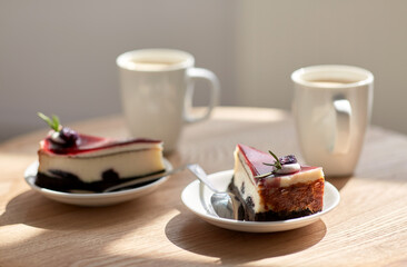 food, junk-food, culinary, baking and holidays concept - pieces of delicious cake on saucers with spoons and coffee cups on wooden table