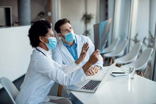 Two doctors cooperating while analyzing X-ray image and wearing face masks due to COVID-19 pandemic.