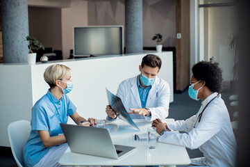 Team of medical experts with face masks analyzing X-ray image during a meeting in hospital.