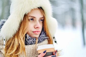 Woman in a fur hat Looks into the distance with a paper cup of coffee in hand. close-up