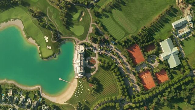 Aerial overhead view of a golf resort with beautiful abstract patterns, sand traps, trees tennis courts, and a turquoise lake. Dolly shot with camera moving forward.