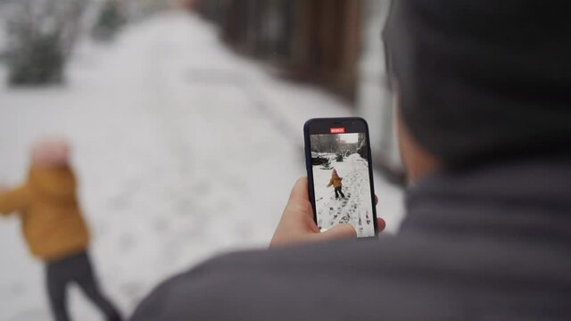 Father taking photo of child with his phone camera. Winter snowy day outdoors
