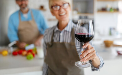Senior couple having fun, cooking and drinking wine in home kitchen