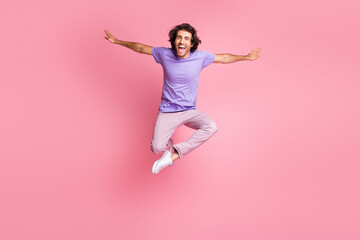 Full size photo of joyful funky guy jump up make hands wings wear pink pants purple t-shirt isolated on bright pink color background