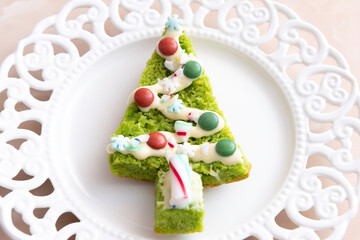 Green cake as a fir with colored candies and white cream on a white plate