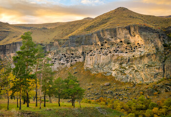 Dramatic Panorama of cave city i Vardzia with trees in foregound on autumn evening during sunset. Balnk space background.