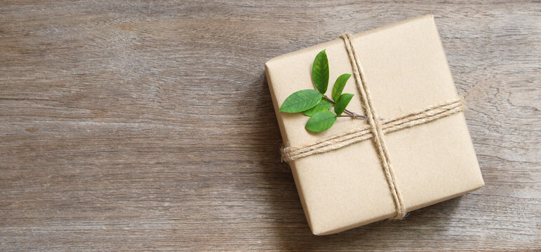gift box wrapped in recycled paper with rope and leaf on wood background with copy space for text or image / green concept
