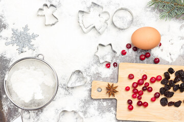 Fototapeta na wymiar Christmas Baking background. Molds, eggs and flour on dark rustic baking tray. Cranberries and raisins on board.