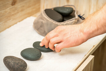 Fototapeta na wymiar Hand of masseur takes hot black massage stones from the table in spa