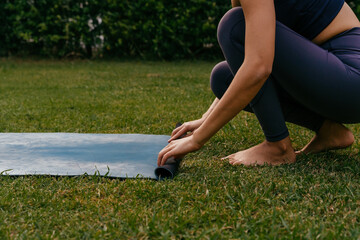 Barefoot female yoga practitioner unrolling mat on grass while preparing for yoga lesson in backyard