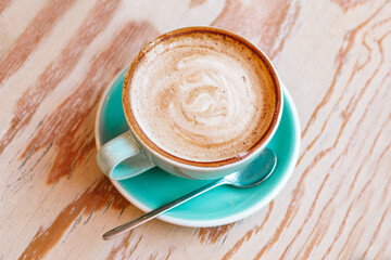 Blue cup with cappuccino on wooden background, top view.