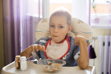 a boy with a bib eats porridge at the children's table
