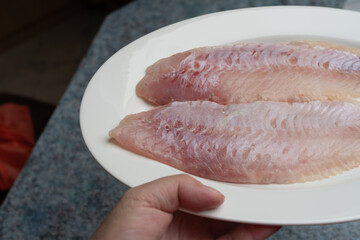 A hand holds a plate with two fillets of freshly caught redfish