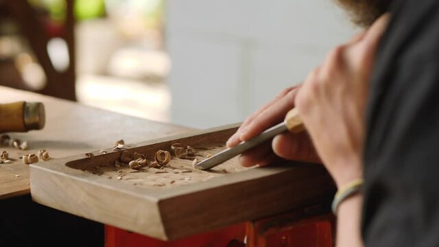 a woodcarver processes a walnut wood board with a chisel. artisan makes a tea tray. vagatabon. tea tray.woodcarver art.