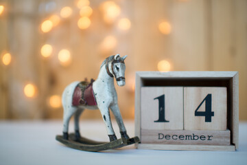 Cube wooden calendar showing date on 14th December with old toy rocking horse over bokeh background. Advent calendar, Christmas background, Copy space