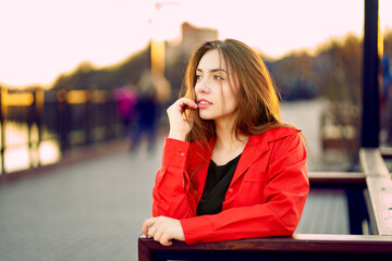 Portrait of a pensive young beautiful woman sitting on a city bridge with a river in the background. Foreground.