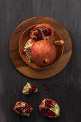 Against a dark background in a wooden bowl lies a ripe and sweet pomegranate