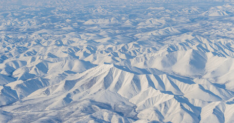 Aerial view of snow-capped mountains and river. Winter snowy mountain landscape. Air travel to the far North of Russia. Mount Nuh, Kolyma Mountains, Magadan Region, Siberia, Russian Far East.