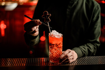 glass with bright ice drink stands on bar and bartender decorates it with candy.