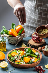 Persimmon salad with spinach, nuts, goat cheese, pomegranate, pumpkin seeds. Freezer food prepare in process vegetarian salad by chef hand in home kitchen. Healthy vegetarian food concept