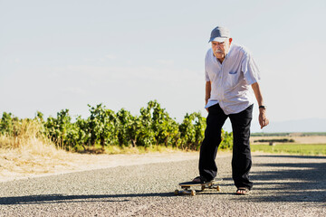 Ottantenne si diverte con ad andare in skateboard in una strada di campagna  