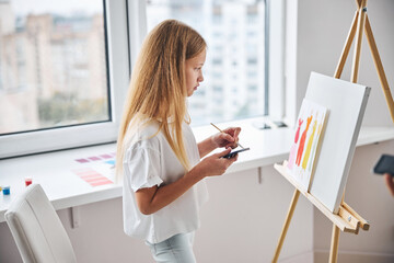 Pupil painting women in dresses on a sheet of paper