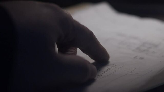 Finger points out details on blueprint  at dark room.