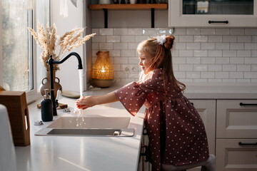 little 5 year old girl washes her hands at home in the kitchen
