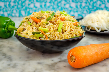 Closeup of Idiyappam Noodles (Indian Rice Noodles) in a black bowl with carrot and capsicum on the side