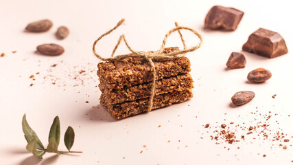 Granola bar with chocolate on a pink background with cocoa beans. Healthy snack, vegan snack