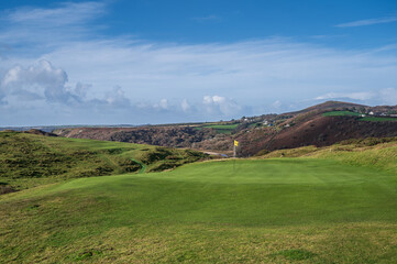 Fototapeta na wymiar A pristine golf green, with the flag in, on a links course on the Welsh coastline. The golf course is Pennard Golf Course over looking the Three Cliffs Bay