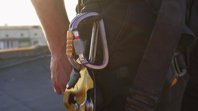 Industrial climber puts a carabiner on climbers belt at summer sunrise. Dangerous work in high-altitude engineering design.