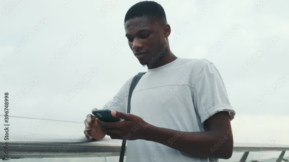 Poster An attractive african american man is standing outside and holding his smartphone in the city