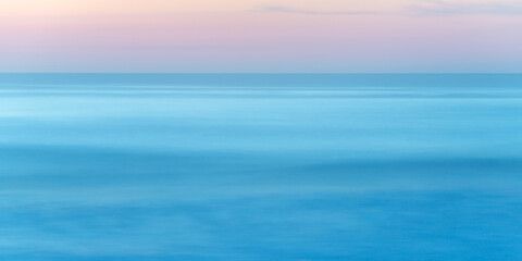 Naklejka na ściany i meble Long exposure of seascape at sunset, blue sea water abstract background, pastel pink sky