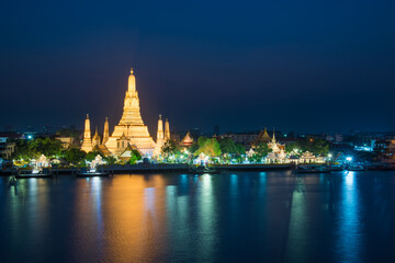 Obraz premium Night illuminated Temple of Dawn or Wat Arun and its reflection in Chao Phraya River at sunset. Bangkok, Thailand