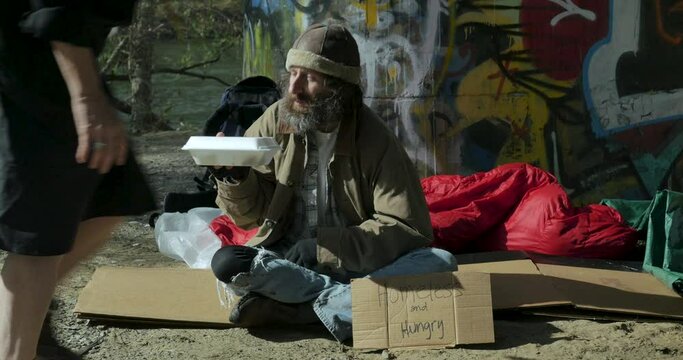 Hungry homeless man getting food from a woman and taking a bite