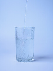 Pouring water from a bottle into a glass on a blue background
