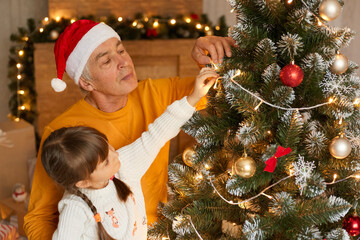 Grandfather and granddaughter decorate fir tree on Christmas eve, looking concentrated at xmas...