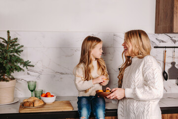 Happy mother with daughter eating mandarins in kitchen