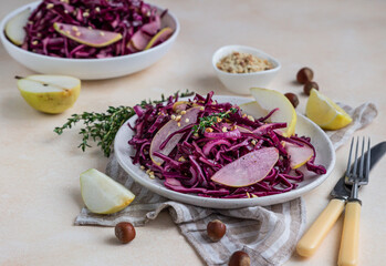 Red cabbage, pear and hazelnut salad with lemon and olive oil sauce. Light stone background. Vegetarian food.