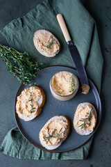 Sandwiches with smoked salmon and soft cream cheese pate or mousse with thyme and rosemary on a ceramic plate, green concrete background. Top view.