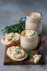 Homemade pate, spread or mousse in glass jar with sliced bread and herbs, light concrete background.