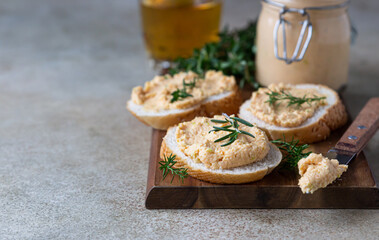 Homemade pate, spread or mousse in glass jar with sliced bread and herbs, light concrete background.