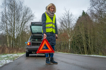 Young blonde woman in a winter down jacket in a yellow vest holds an emergency stop sign an orange...