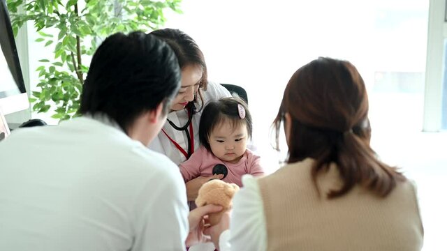 両親に見守られながら赤ちゃんが女性医師の診察を受けている。