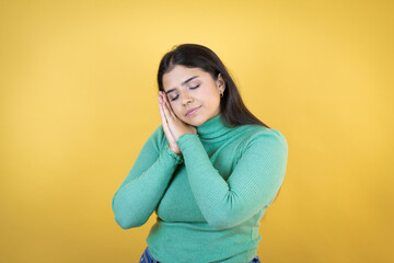 Young caucasian woman over isolated yellow background sleeping tired dreaming and posing with hands together while smiling with closed eyes.