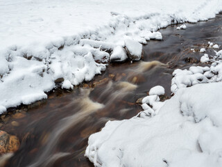 Winter mountain stream in Karelia flows through the forest. The power of wild majestic nature. Water turbulence.