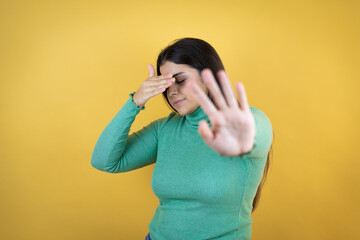 Young caucasian woman over isolated yellow background covering eyes with hands and doing stop gesture with sad and fear expression. Embarrassed and negative concept.