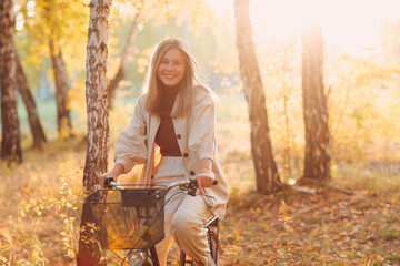 Happy active young woman riding vintage bicycle in autumn park at sunset